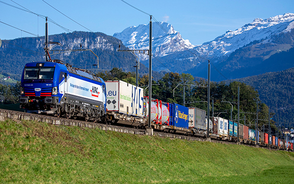 Un train de marchandises passe devant un paysage alpin.